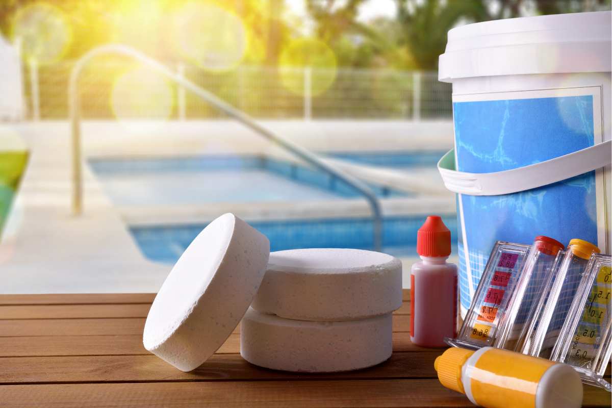 swimming pool service equipment and chemical cleaning products and tools on a wooden table and pool background.