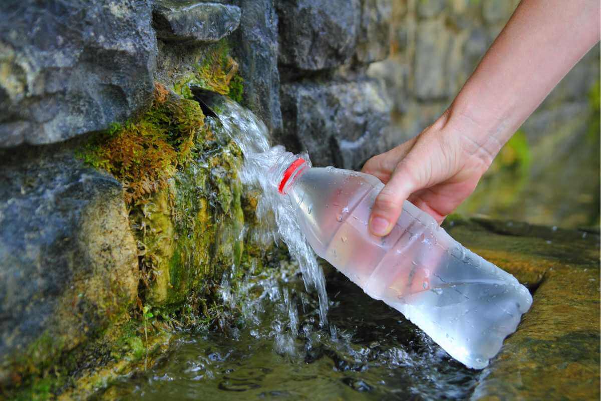 A source of spring water, someone holds a bottle to fill it up from the spring